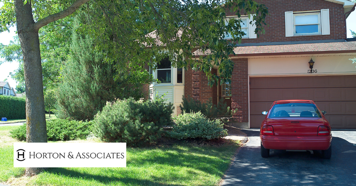 Red car parked in driveway of suburban home, representing combined home and auto insurance with Horton & Associates.
